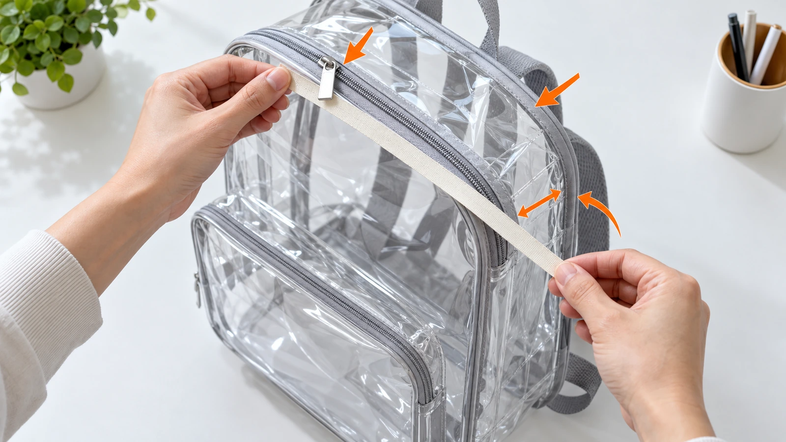 Düz bir metre ile şeffaf PVC sırt çantasının dış yüksekliğini, genişliğini ve körük derinliğini ölçen eller; oklar, fermuar tutacaklarının ve kenar bandının boyuta dahil edildiğini gösterir
