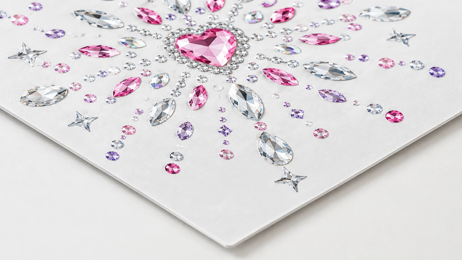 Rhinestone motifinin yakın çekimi Beyaz bir levha üzerinde şeffaf, pembe ve mor taşlardan oluşan, pembe kalp merkezli rhinestone motifinin yakın çekimi
